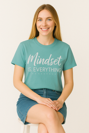 Chalky Mint Comfort Colors tee with “Mindset Is Everything” quote in gold and white font. Worn by woman sitting peacefully.