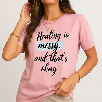 Pink Comfort Colors t-shirt with “Healing is messy and that’s okay” quote. Mental health tee worn by woman with gold accessories.
