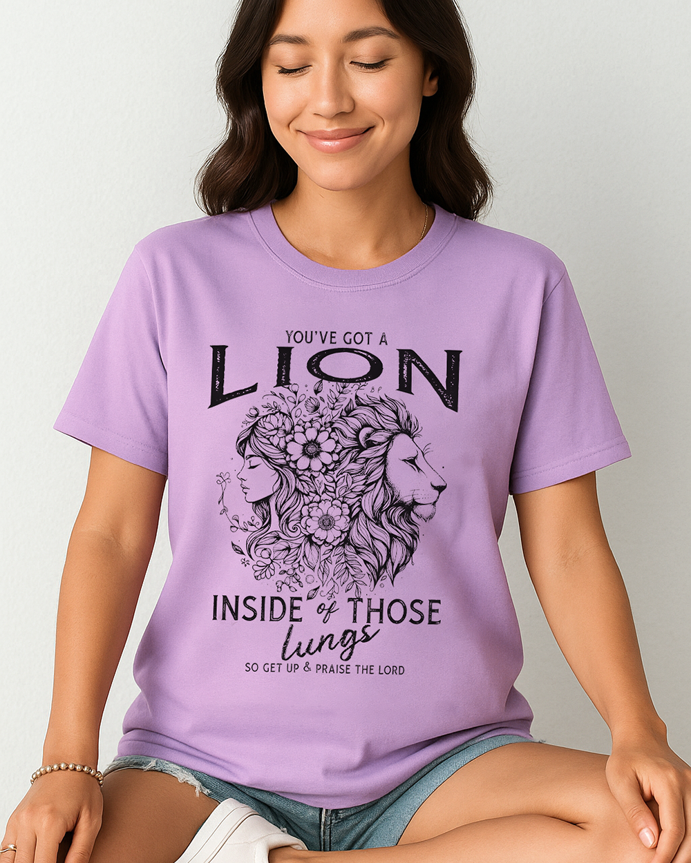 Orchid Comfort Colors tee with “You’ve Got a Lion Inside of Those Lungs” quote and lion-woman floral artwork. Worn by seated woman in shorts.