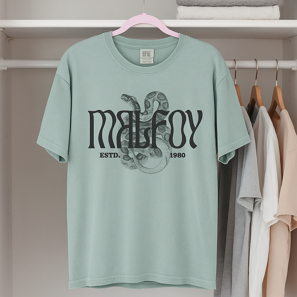 Malfoy snake graphic tee in Bay green, laid flat on white bedding