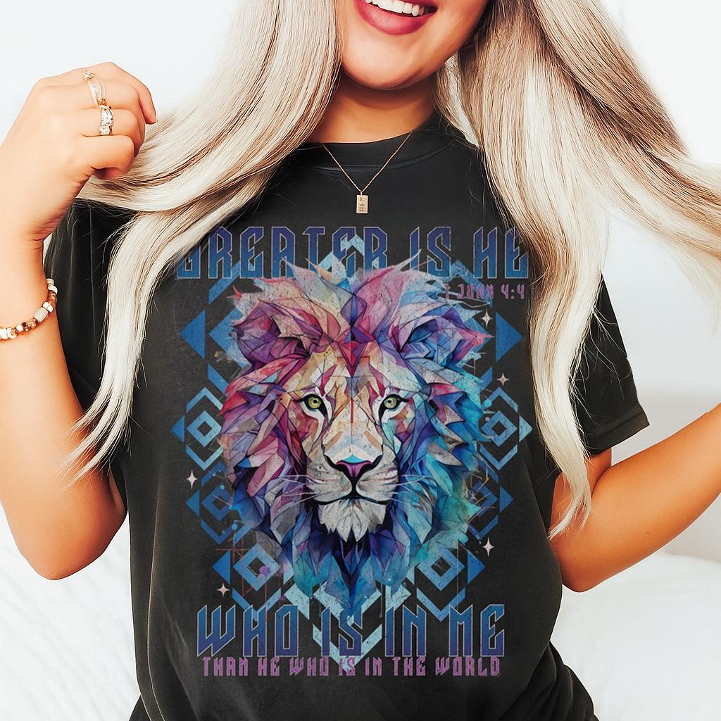 Woman wearing an ivory Comfort Colors Christian shirt with colorful lion art and verse “Who is in me” from 1 John 4:4.