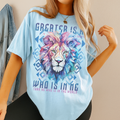 Model in chambray blue Comfort Colors t-shirt featuring vibrant geometric lion face and scripture “Greater Is He” – Christian faith tee.