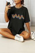 Black Comfort Colors t-shirt with rainbow “Healing is not linear” quote. Worn by woman sitting on floor.