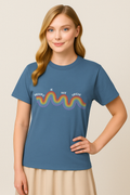 Blue Jean Comfort Colors t-shirt with rainbow “Healing is not linear” quote. Worn by blonde woman standing casually.