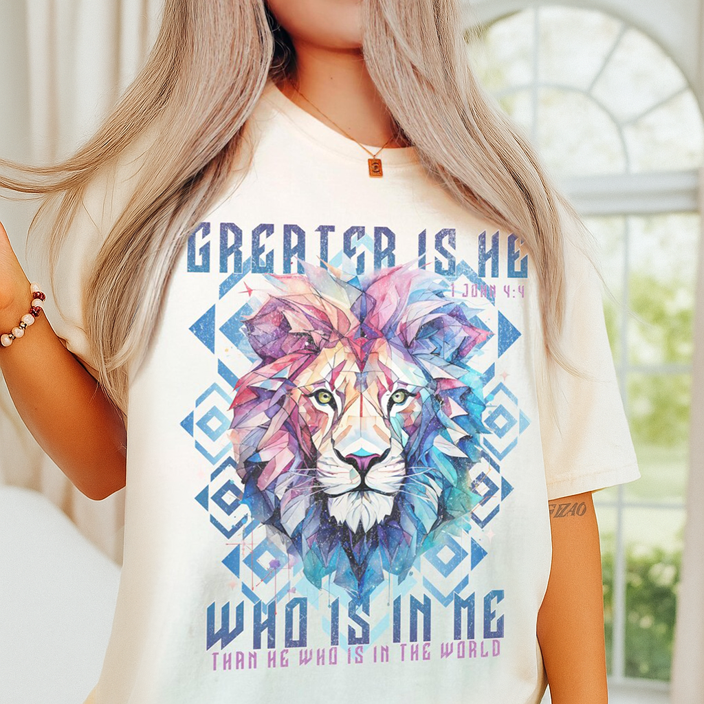 Woman wearing an ivory Comfort Colors Christian shirt with colorful lion art and verse “Who is in me” from 1 John 4:4.