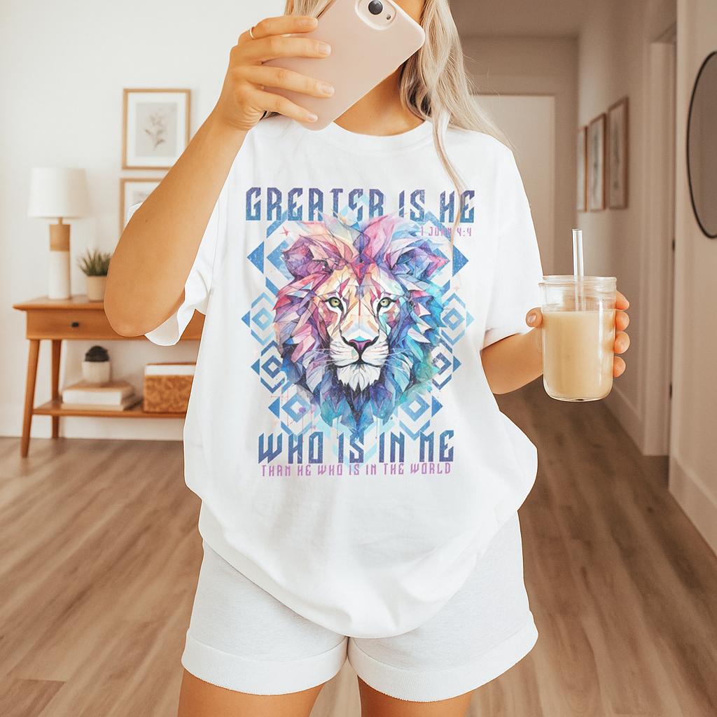 Woman in a bright white Jesus shirt, holding iced coffee, with vibrant lion face and scripture text “Greater is He” – cozy Christian morning outfit.