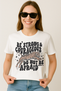 White Comfort Colors t-shirt with “Be Strong & Courageous” scripture and tiger design. Worn with sunglasses and relaxed denim.