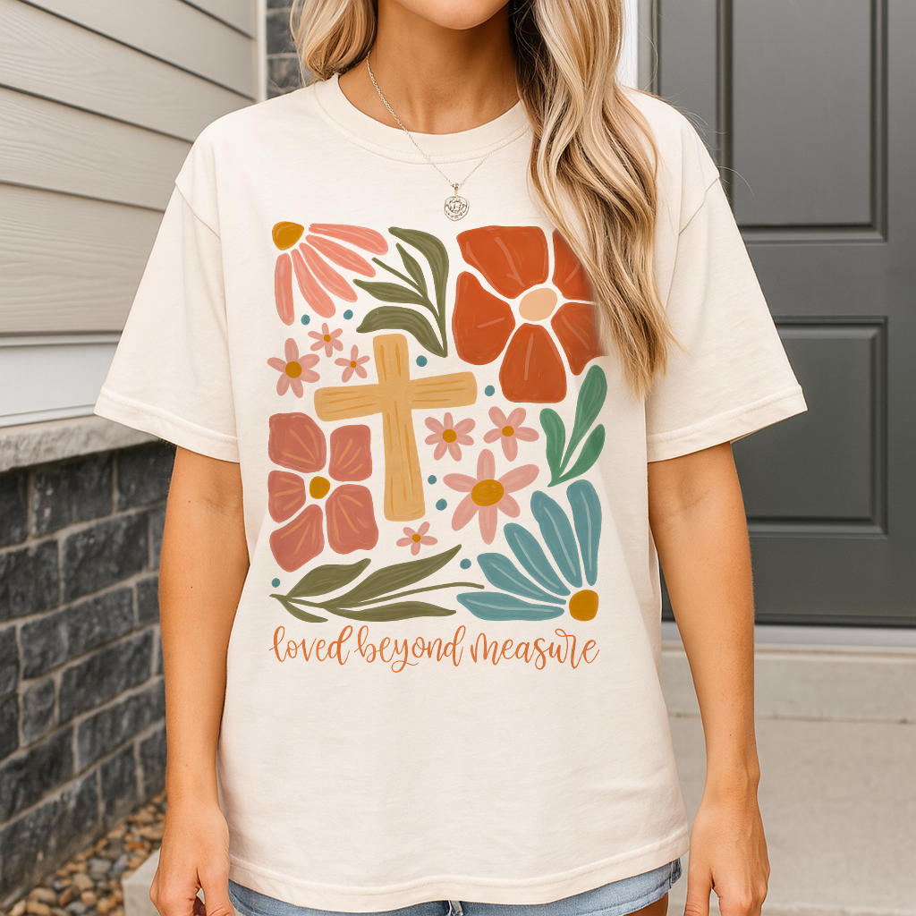 Soft ivory Christian tee with hand-drawn flower bouquet, cross, and “Loved Beyond Measure” script